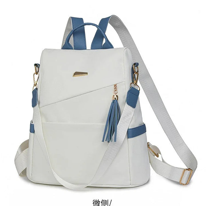 White backpack with blue straps, gold zipper and tassel charm, adjustable white shoulder strap
