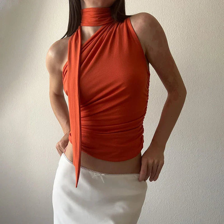 woman wearing sleeveless rust orange top with neck scarf paired with white skirt against white wall