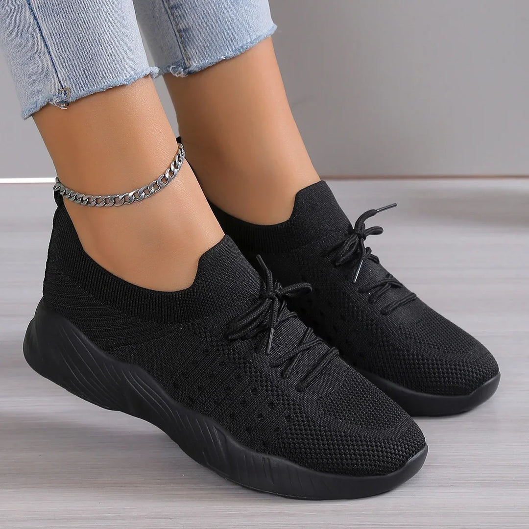 Black knit sneakers with thick soles worn with cropped light blue jeans and a silver ankle chain