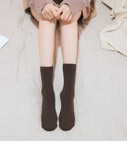 Person wearing brown socks sitting on a beige fabric surface with hands clasped over knees