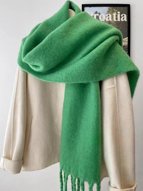 Soft green wool scarf draped over cream wool coat on hanger against white wall with Croatia poster