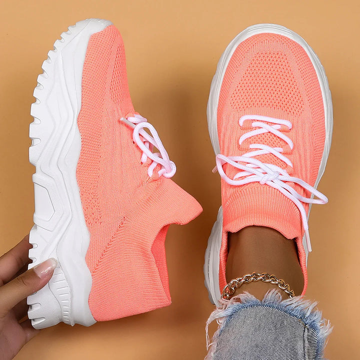 Trendy coral pink knit sneakers with white chunky soles and laces on beige background