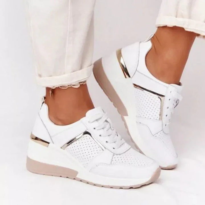 White perforated platform sneakers with metallic gold accents worn with rolled-up white pants