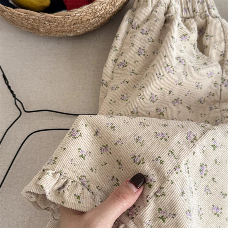 Close-up of beige corduroy fabric with small purple floral print and ruffled edge, held by hand
