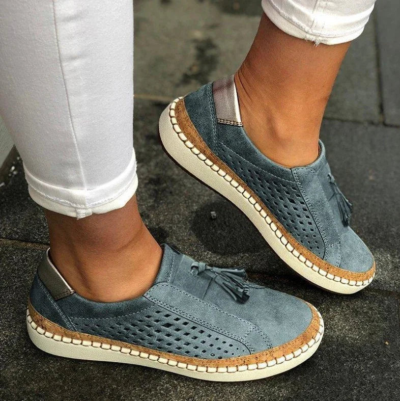 Blue suede casual perforated sneakers with tassels and cork trim worn with white pants on pavement