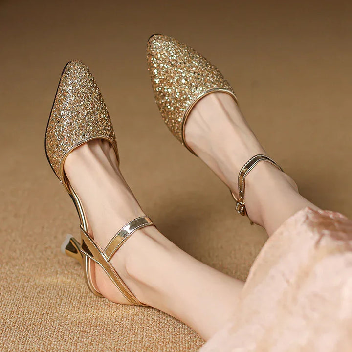 Women's sparkling gold glitter pointed-toe slingback heels with ankle straps on beige carpet
