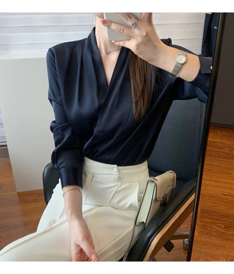 Woman wearing navy blue blouse and white high-waisted pants sitting on chair with beige handbag