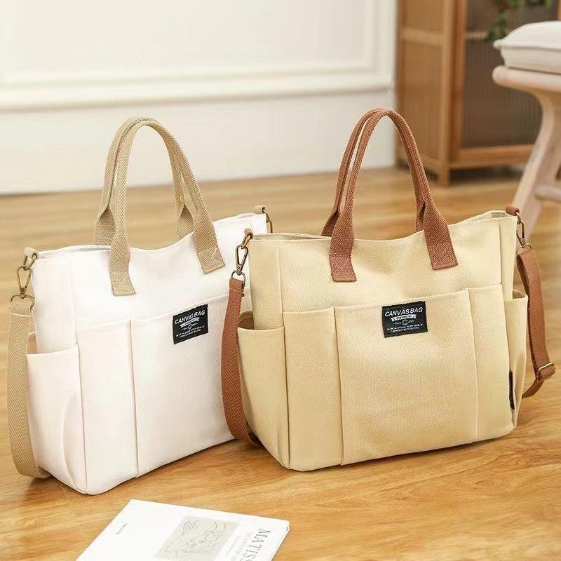 Two canvas tote bags with multiple pockets and shoulder straps on wooden floor, beige and white colors