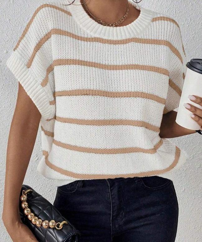 Woman wearing white and beige striped knit sweater vest with black pants, holding black quilted handbag and coffee cup