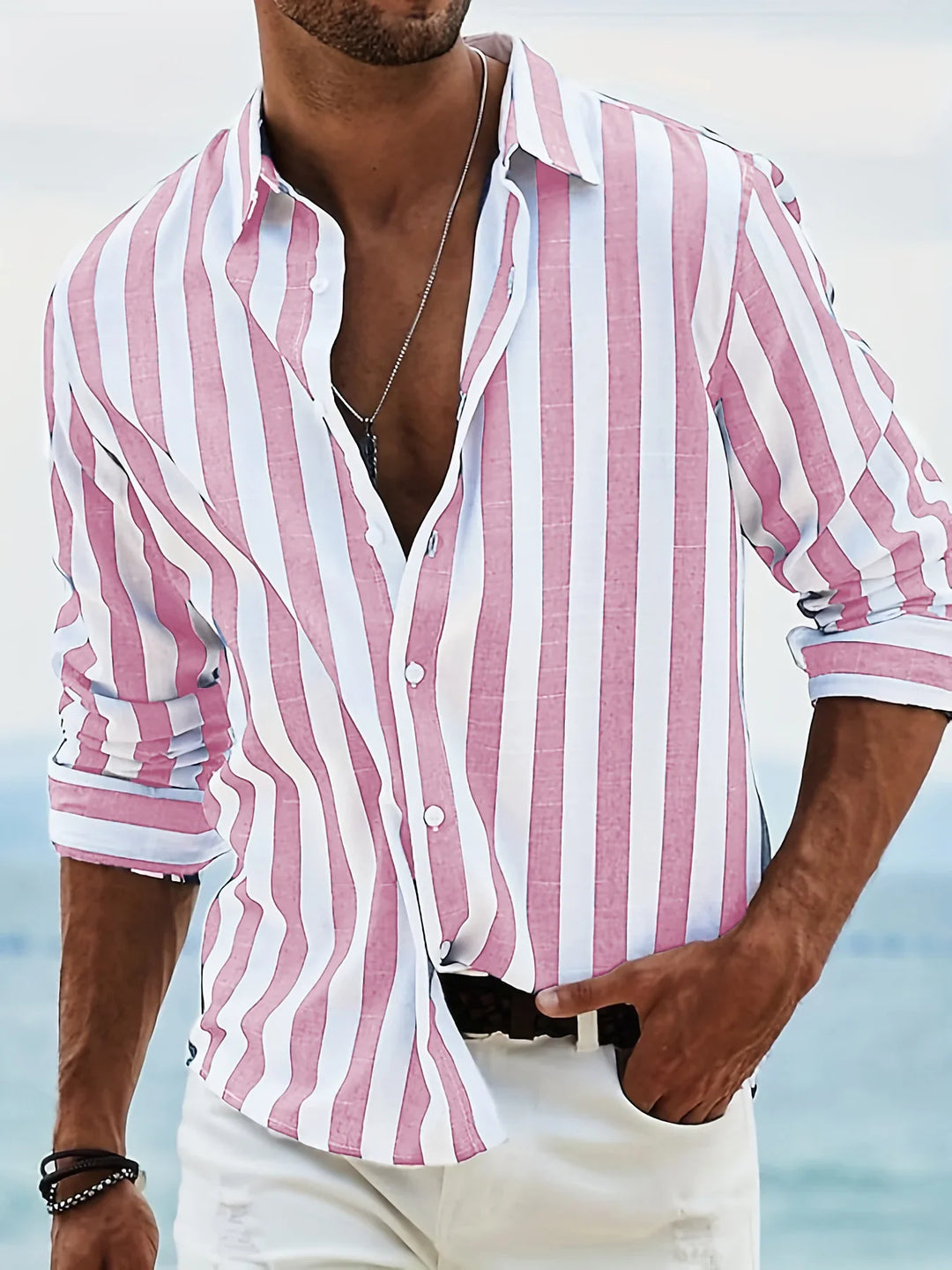 Man wearing pink and white striped button-down shirt with rolled sleeves at the beach