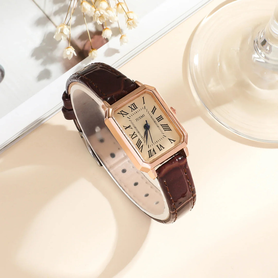 Elegant rectangular rose gold watch with Roman numerals and brown leather strap on beige surface