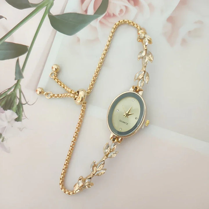 Elegant gold bracelet watch with oval face and leaf-shaped embellishments on a floral background