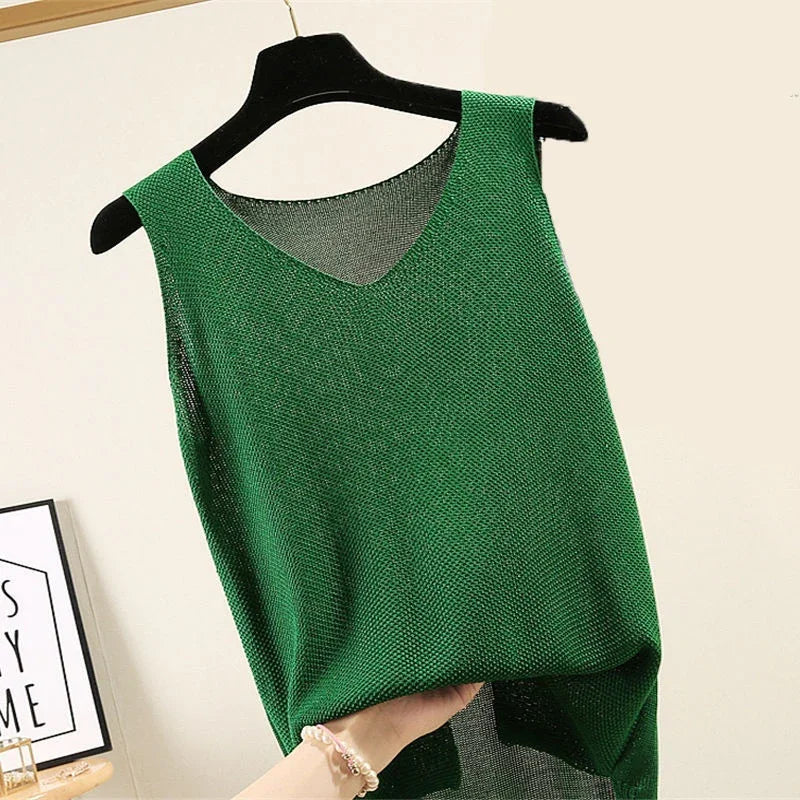 Hand holding green sleeveless textured knit top on black hanger against beige wall