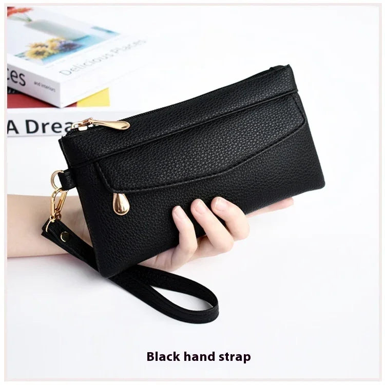 Black textured leather wristlet clutch with gold zipper and hand strap, held in hand