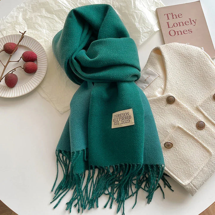 Green wool scarf with fringe and label, beige textured jacket with buttons, plate with lychee fruits on white table