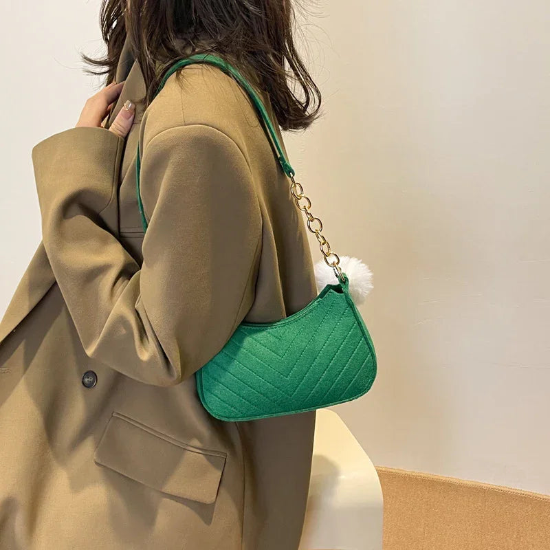 Woman wearing camel blazer carrying green quilted shoulder bag with gold chain and white pom pom