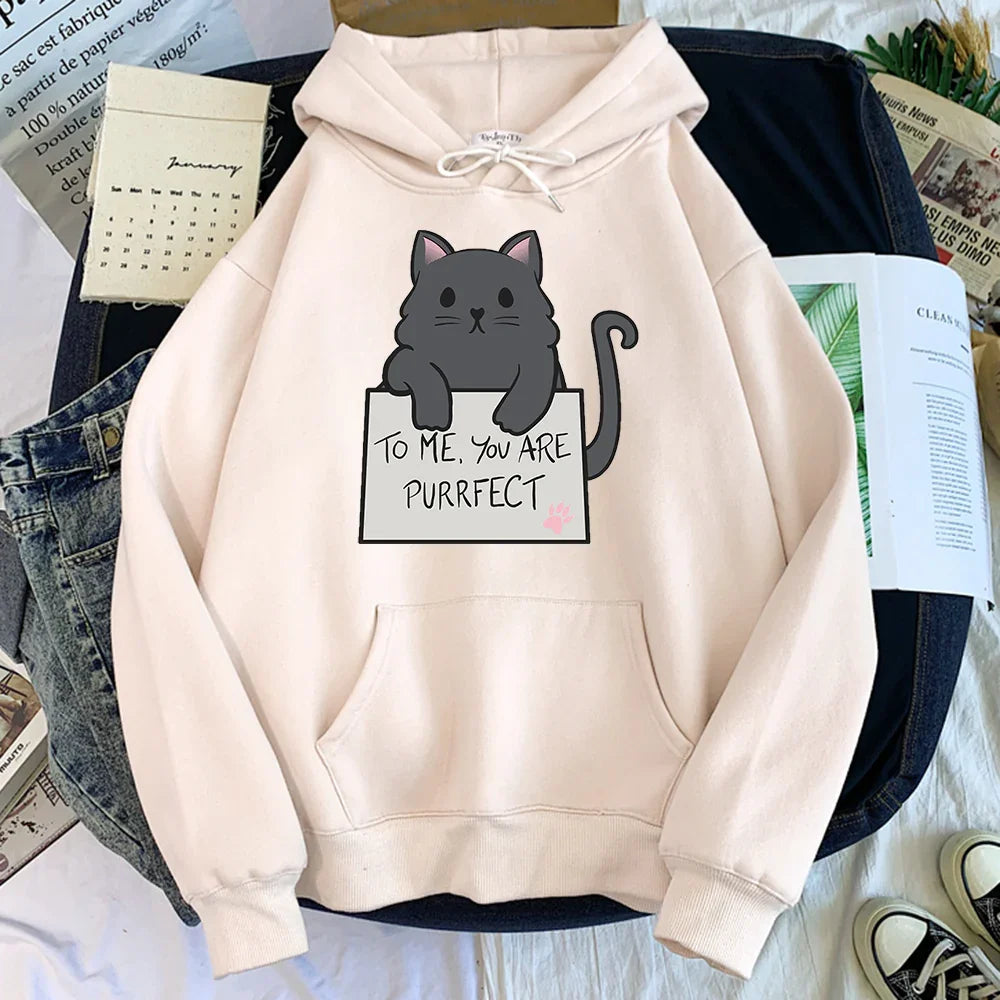 Light beige hoodie with a cute black cat graphic holding a sign saying 'To me, you are purrfect' laid on denim jeans and jacket