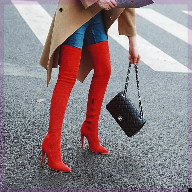 Woman wearing red over-the-knee high heel boots, blue jeans, beige coat, holding black quilted handbag