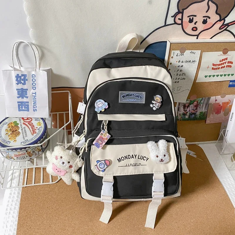 Black and beige Monday Lucy backpack with cute space and animal pins on a desk with snacks and bulletin board