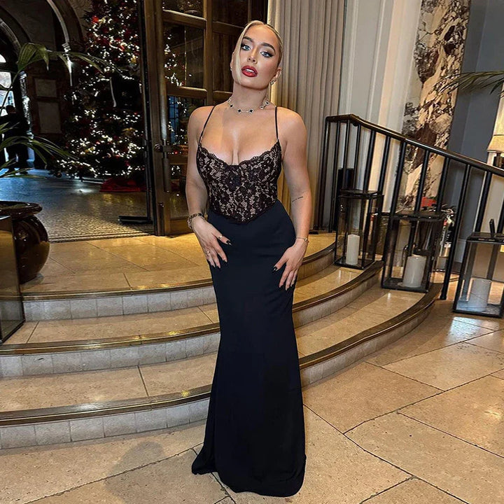 Elegant woman in a black lace bodice evening gown standing indoors by curved staircase with holiday decor