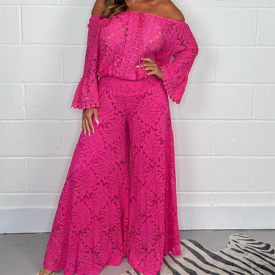 Woman wearing hot pink lace off-shoulder top and wide-leg pants against white brick wall