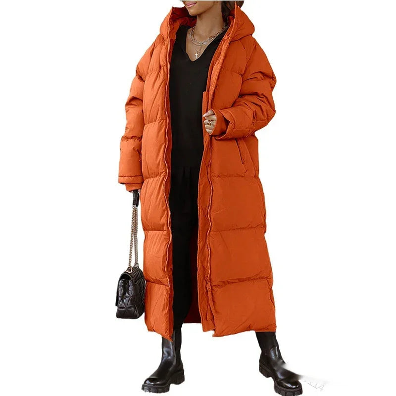 Woman wearing long orange puffer coat with hood, black outfit, boots, and holding black quilted handbag