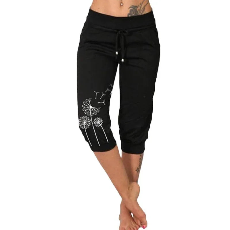 Black cropped casual pants with white dandelion print on side, worn by a barefoot woman