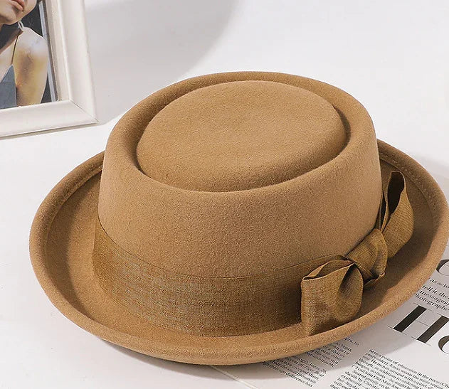 Brown wool fedora hat with matching fabric band and bow detail on white surface with magazine and framed photo