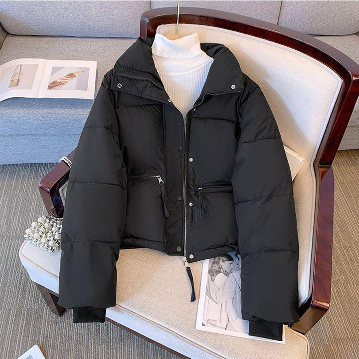 Black puffer jacket with silver zipper and snap buttons on chair over white turtleneck sweater