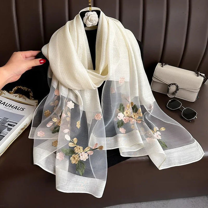 Elegant white sheer scarf with floral embroidery displayed on black mannequin with handbag and sunglasses