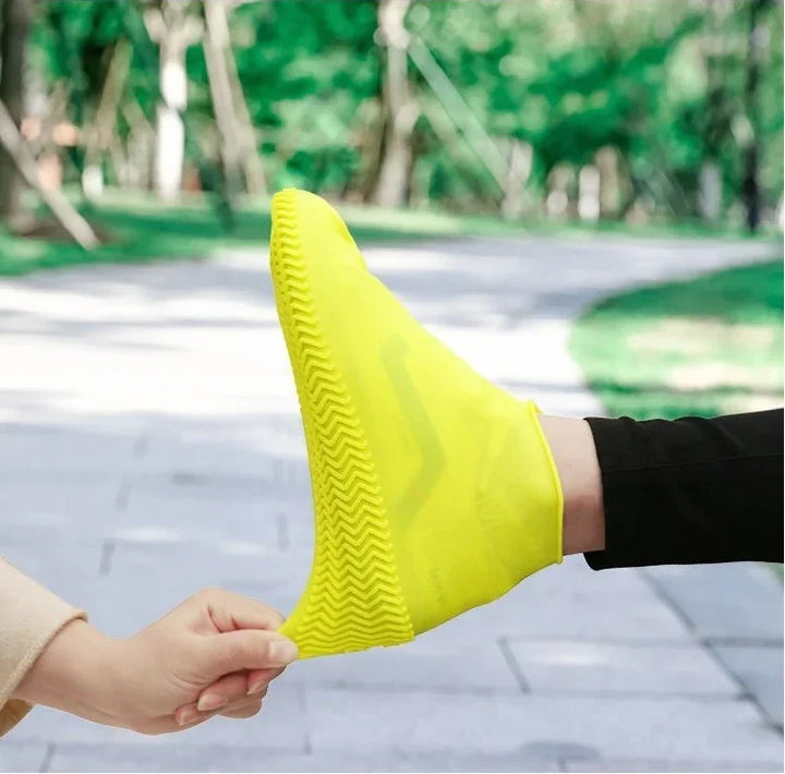 Person wearing and stretching bright yellow waterproof shoe cover outdoors on pavement path
