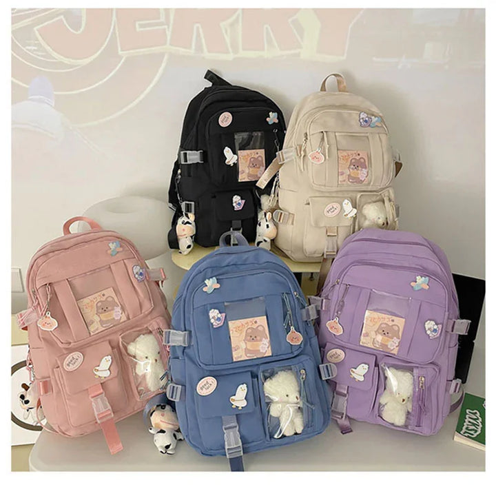 Five colorful backpacks in black, beige, pink, blue, and purple with cute animal patches and stuffed toys