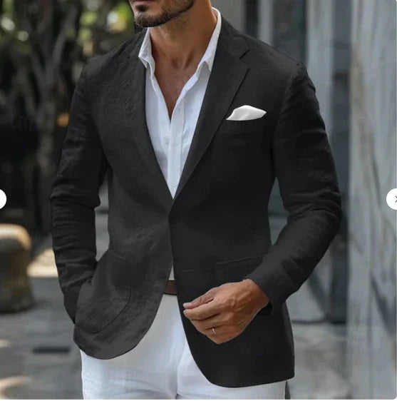 Man wearing black blazer with white pocket square over white shirt and white pants outdoors
