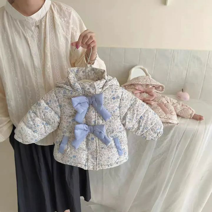 Woman holding a floral baby jacket with blue bows, a pink floral baby jacket lies on a sofa