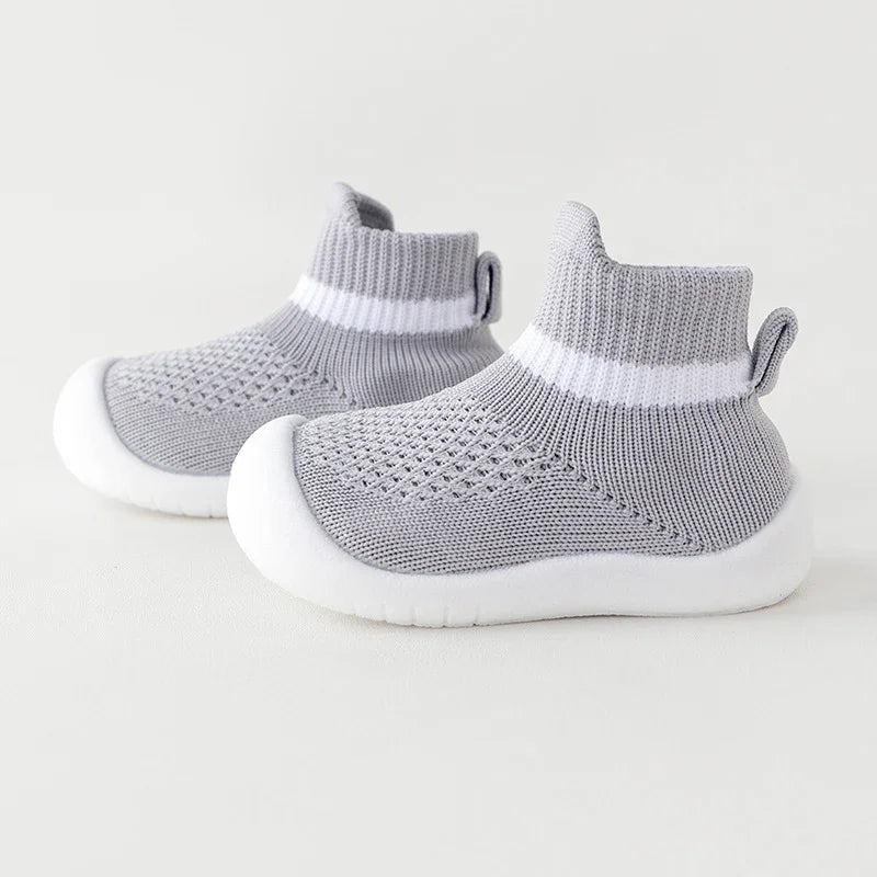Light grey knitted baby shoes with white soles and ankle cuffs featuring a white stripe