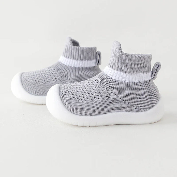 Light grey knitted baby shoes with white soles and ankle cuffs featuring a white stripe