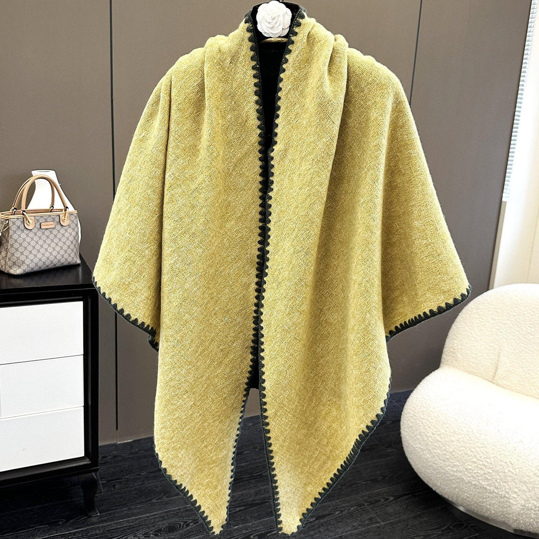 Yellow wool cape with black trim, displayed on mannequin in modern room with white chair and gray cabinet