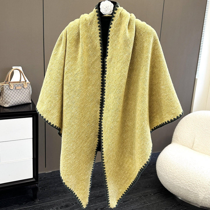Yellow wool cape with black trim, displayed on mannequin in modern room with white chair and gray cabinet