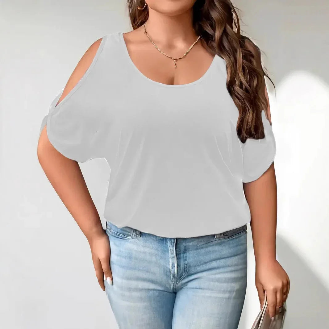 Woman wearing white cold shoulder top and light blue jeans holding a beige purse