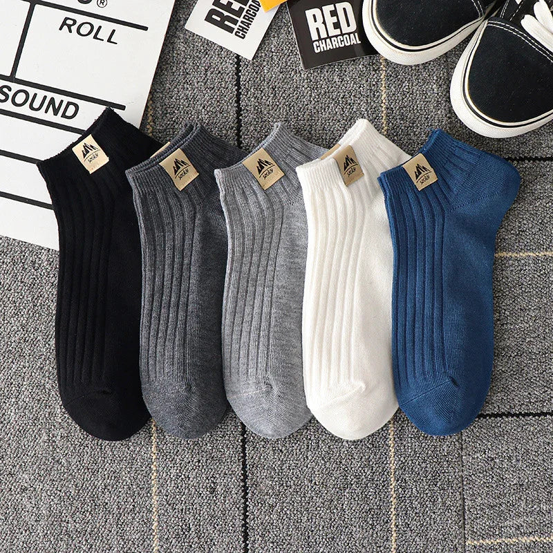 Set of five ribbed ankle socks in black, dark gray, light gray, white, and blue on gray carpet with sneakers and paper tags