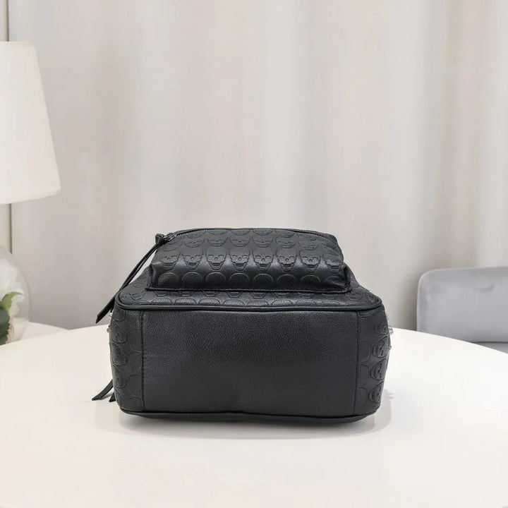 Black leather backpack with embossed skull pattern on white table in minimalist room