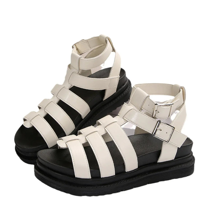 White strappy gladiator sandals with black thick soles and silver buckles on white background