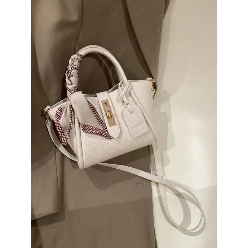 White textured leather handbag with gold hardware and a patterned scarf wrapped around the handle