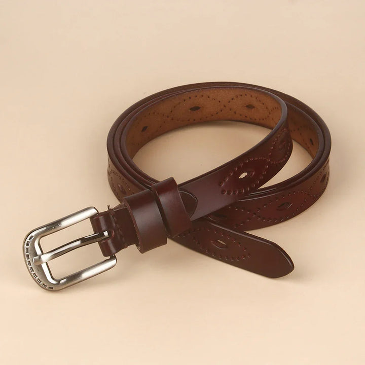 Rolled brown leather belt with decorative perforated patterns and silver buckle on beige background
