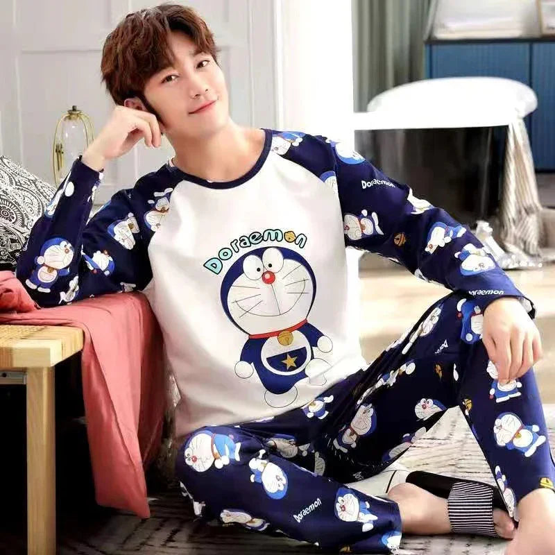 Young man wearing blue and white Doraemon pajamas sitting on the floor next to a bed with patterned pillows