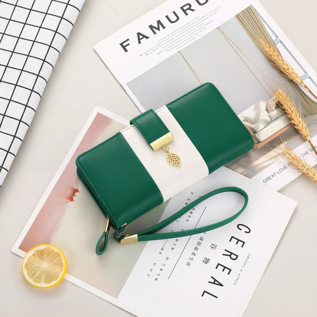 Green and white leather wristlet wallet with gold leaf charm on styled magazines and wheat decor
