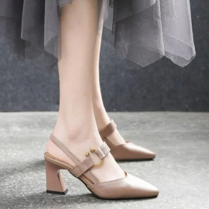 Wearing beige pointed toe slingback block heel shoes with gold buckle detail on gray floor