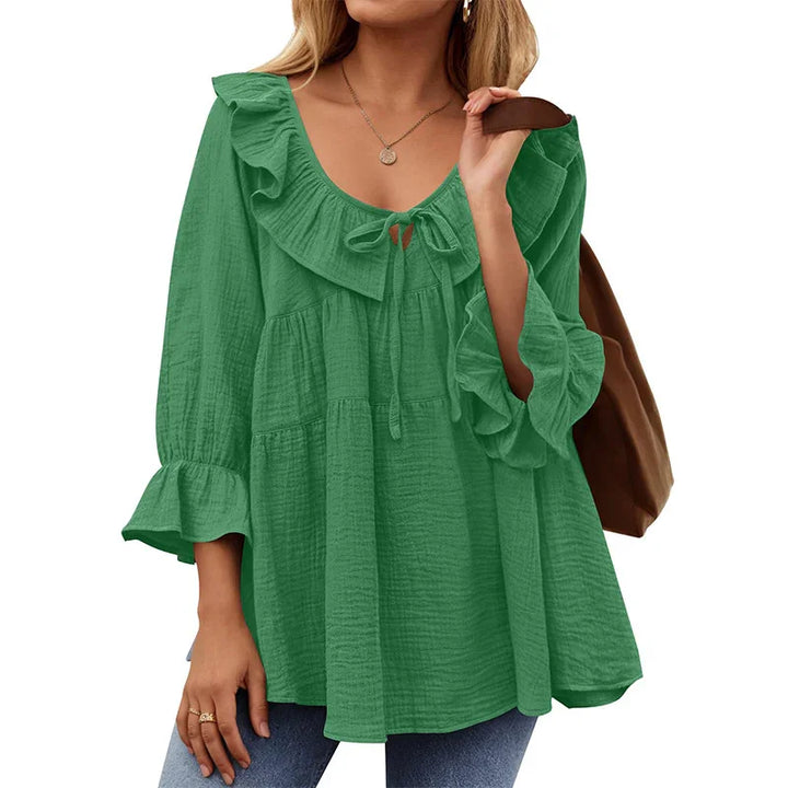 Woman wearing green ruffled blouse with tie neckline and 3/4 bell sleeves, carrying brown bag