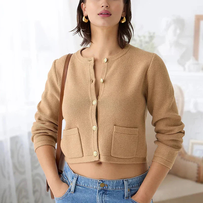 Woman wearing a cropped beige cardigan with gold buttons and front pockets, paired with blue jeans