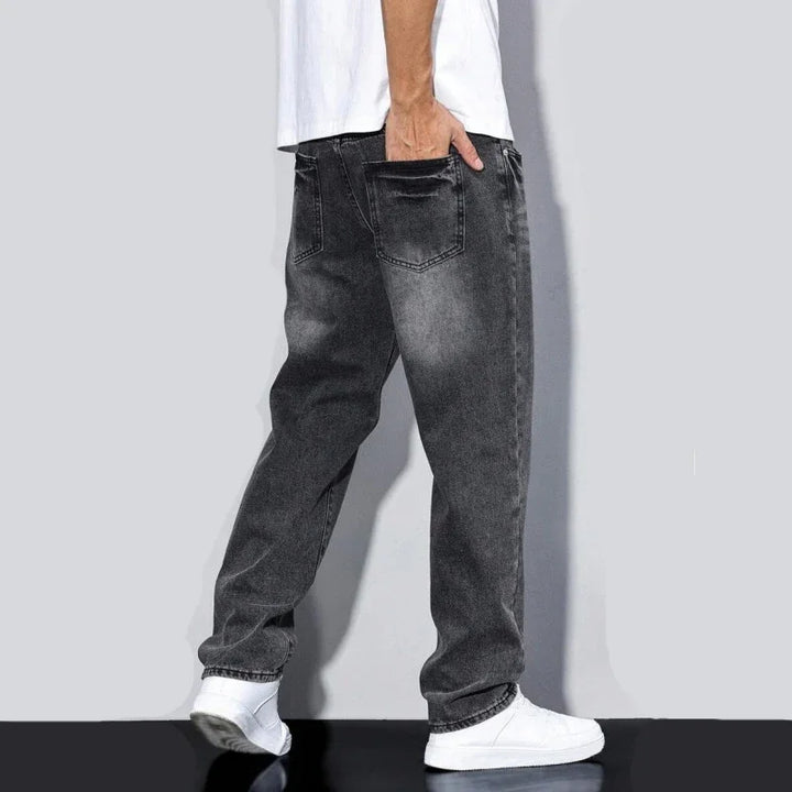 Man wearing faded black baggy jeans and white sneakers against gray background
